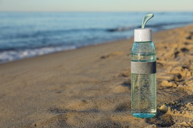 Photo of Glass bottle with water on wet sand near sea. Space for text