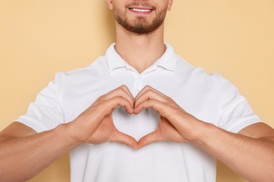 Photo of Happy volunteer making heart with his hands on beige background, closeup