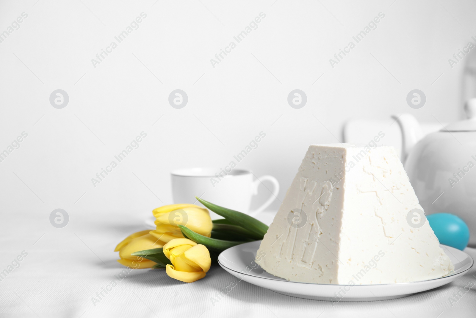 Photo of Traditional cottage cheese Easter paskha and yellow tulips on white fabric, space for text