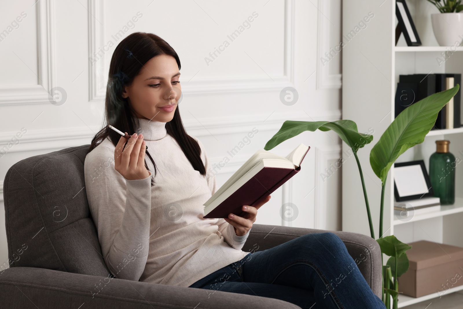 Photo of Woman using cigarette holder for smoking while reading book indoors