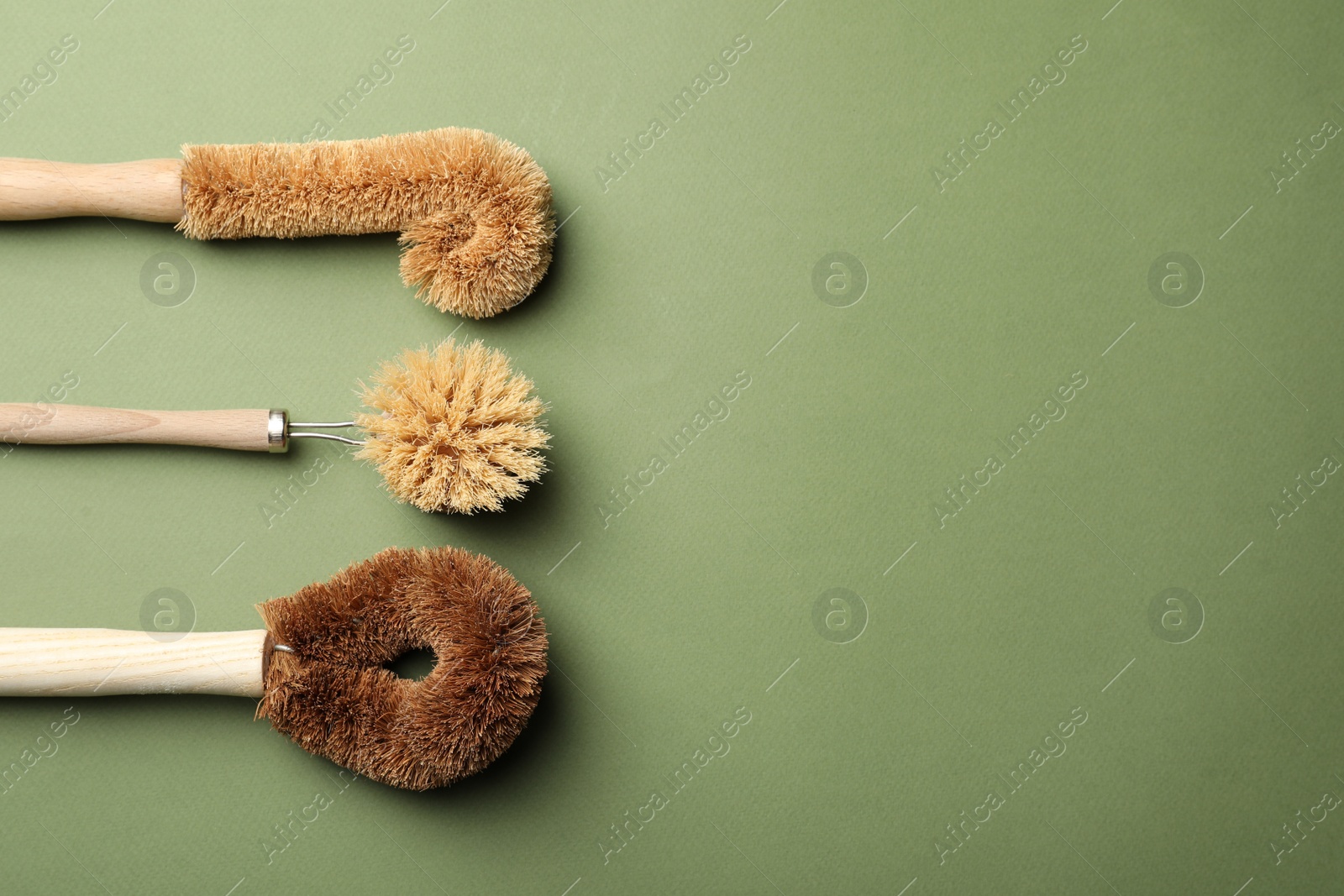 Photo of Different bamboo brushes for dish washing on green background, flat lay. Conscious consumption