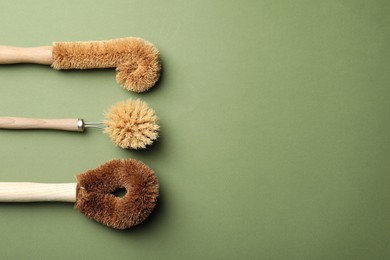 Different bamboo brushes for dish washing on green background, flat lay. Conscious consumption