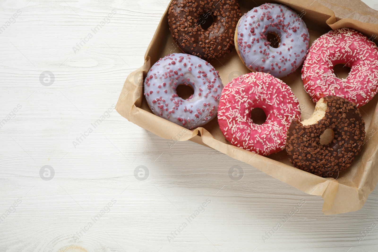 Photo of Delicious glazed donuts on white wooden table, top view. Space for text
