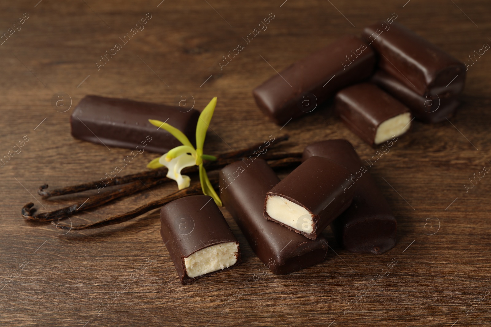 Photo of Glazed curd cheese bars, vanilla pods and flower on wooden table