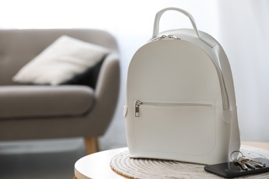 Stylish white backpack, smartphone and keys on wooden table in living room, space for text