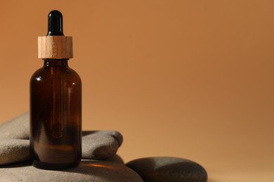 Photo of Bottle of face serum and spa stones on beige background, closeup. Space for text