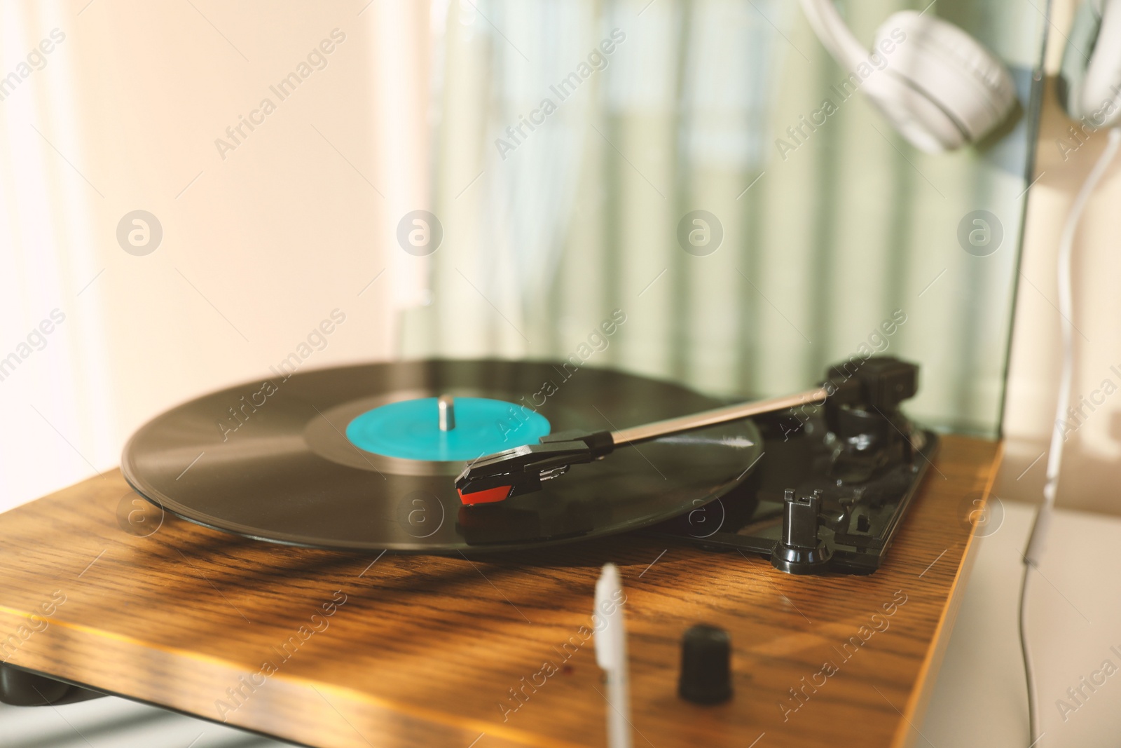 Photo of Stylish turntable with vinyl disc and headphones on white table at home, closeup