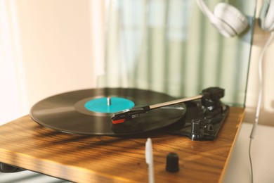 Stylish turntable with vinyl disc and headphones on white table at home, closeup