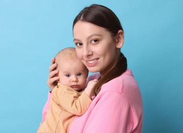 Happy mother with her cute baby on light blue background