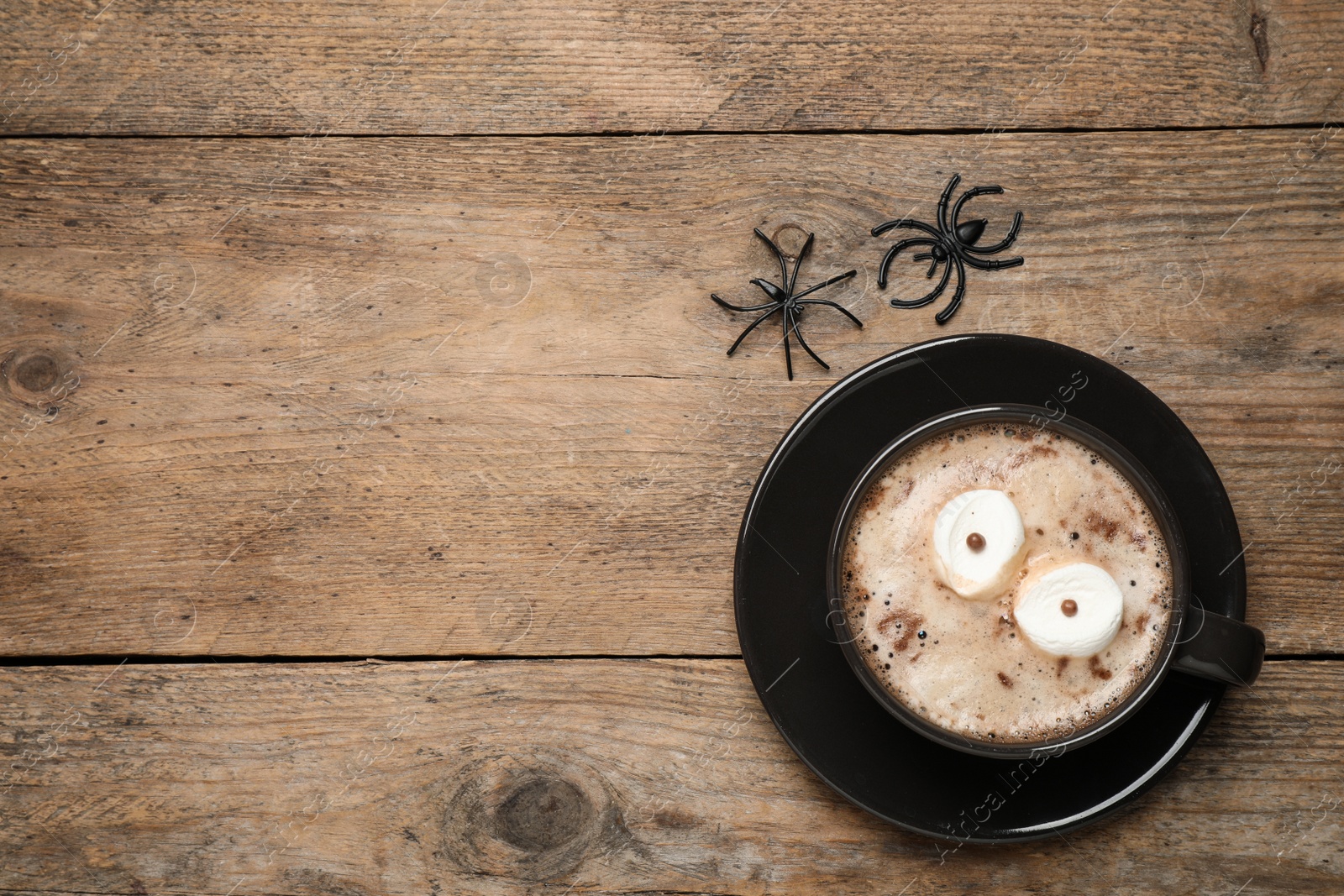 Photo of Cup of coffee decorated with marshmallow eyes and space for text on wooden table, flat lay. Halloween celebration