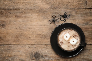 Cup of coffee decorated with marshmallow eyes and space for text on wooden table, flat lay. Halloween celebration