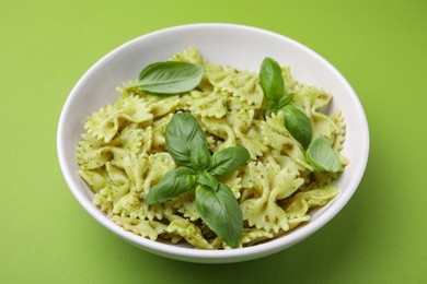 Photo of Delicious pasta with pesto sauce and basil on light green background, closeup