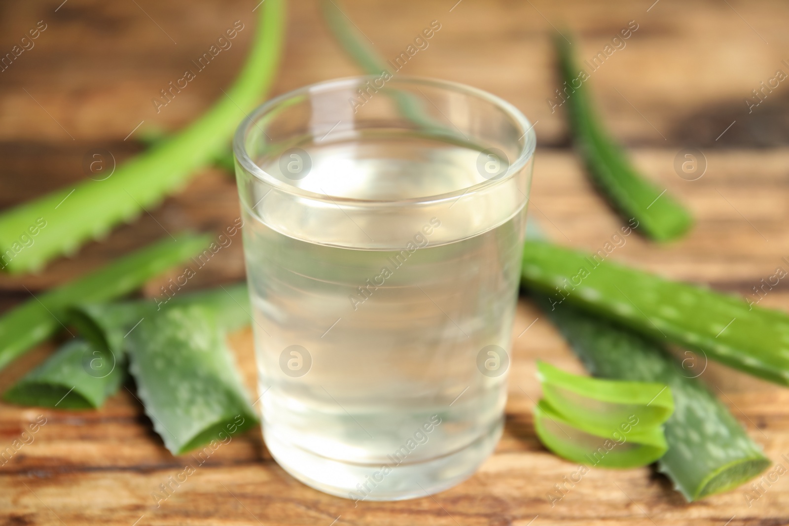 Photo of Fresh aloe drink in glass and leaves on wooden table