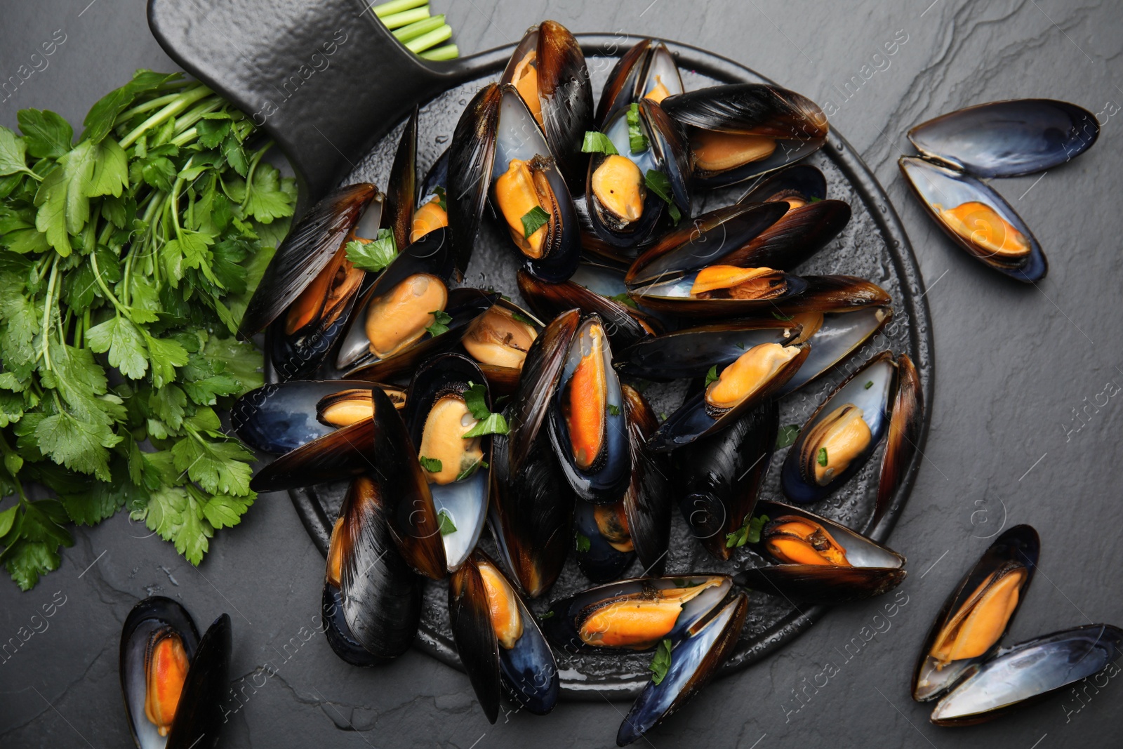 Photo of Serving board with cooked mussels and parsley on slate table, flat lay