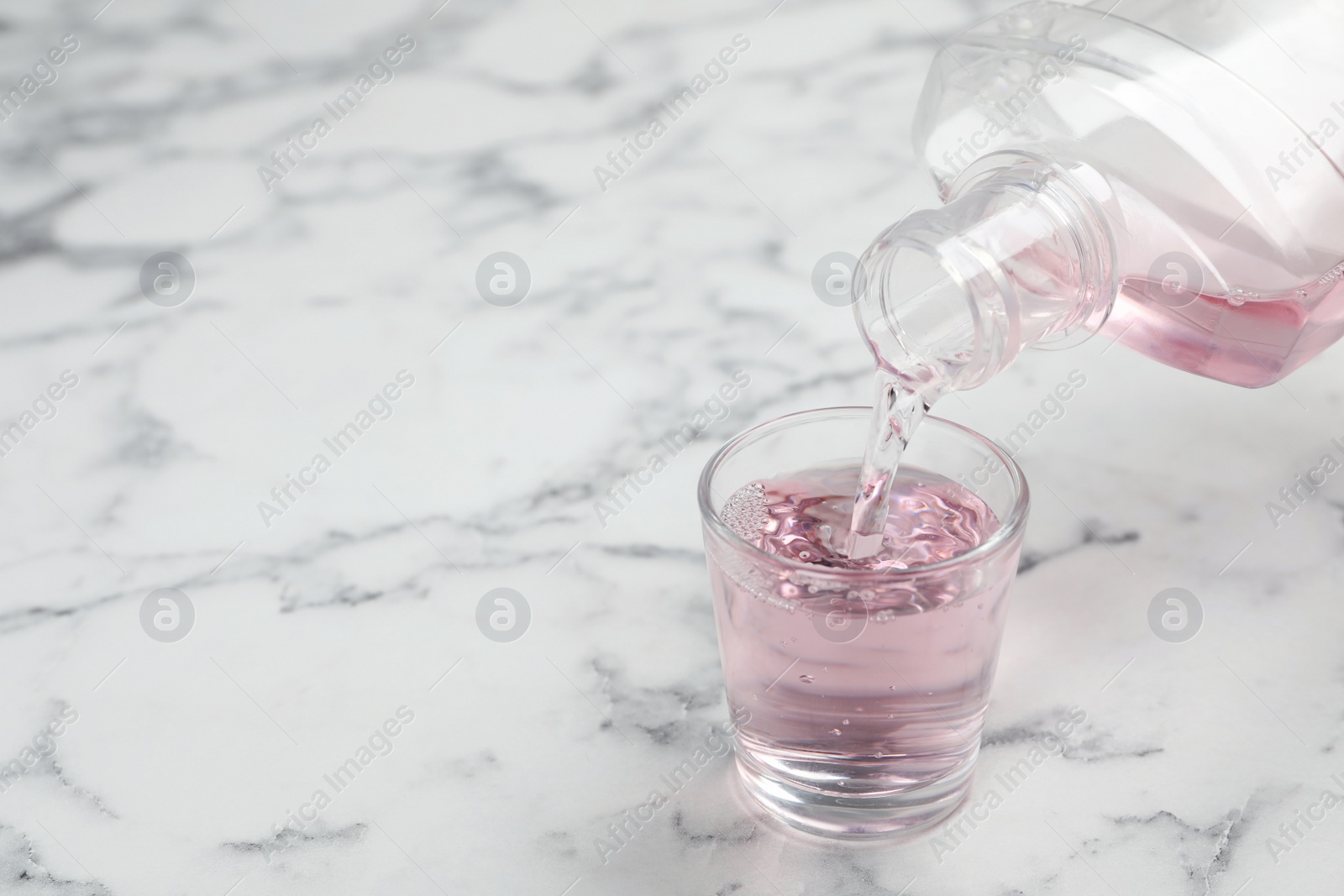 Photo of Pouring mouthwash in glass and space for text on marble background. Teeth care