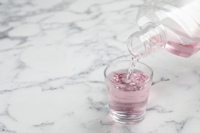 Photo of Pouring mouthwash in glass and space for text on marble background. Teeth care