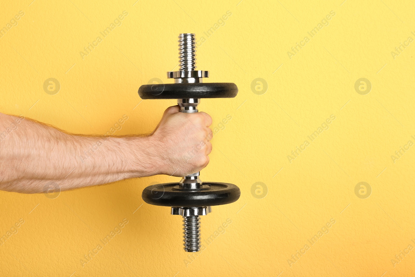 Photo of Male athlete holding metal dumbbell on color background. Space for text