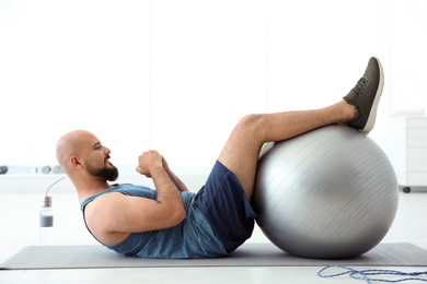 Overweight man doing exercise with fitness ball in gym