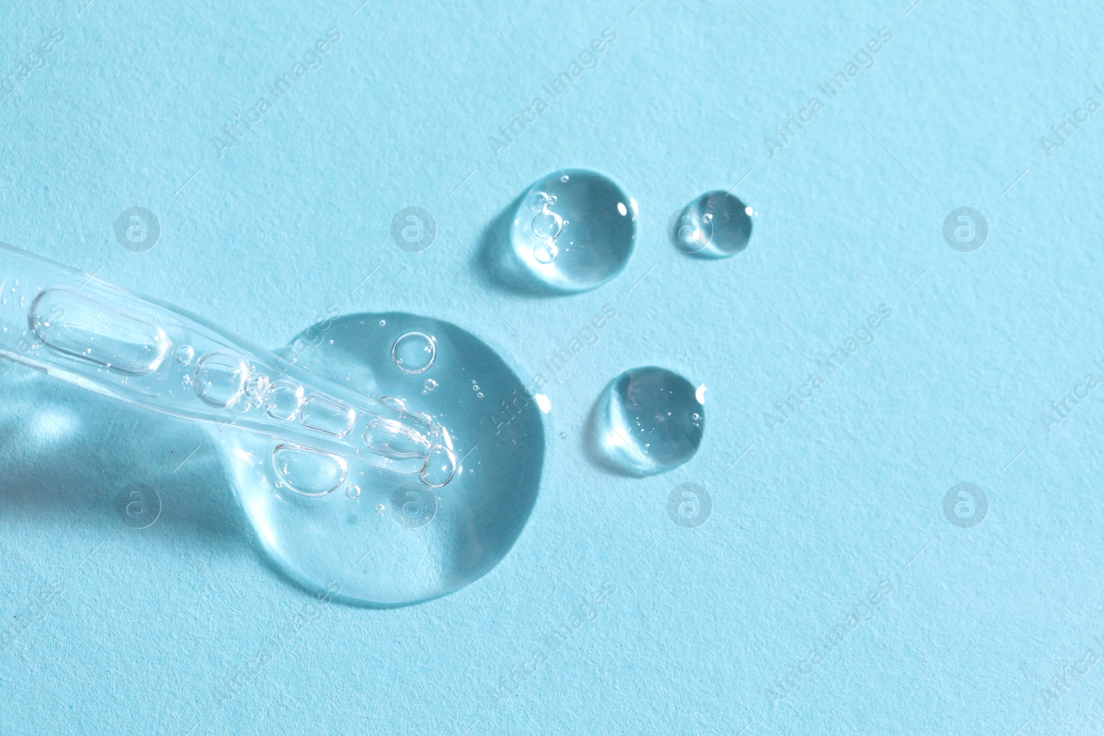 Photo of Glass pipette and transparent liquid on light blue background, top view. Space for text