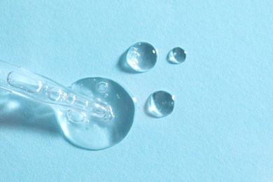 Photo of Glass pipette and transparent liquid on light blue background, top view. Space for text