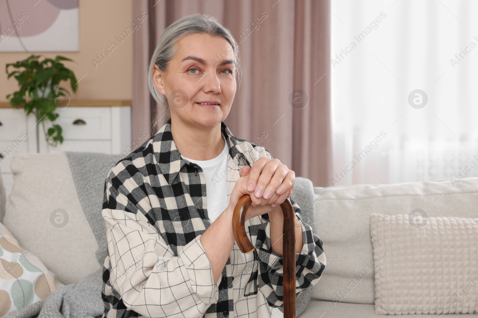 Photo of Senior woman with walking cane sitting on sofa at home. Space for text