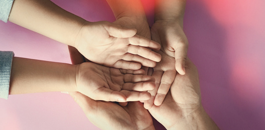 Happy family holding hands on pink background, top view. Banner design 