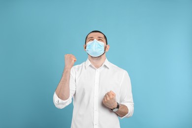 Photo of Emotional man with protective mask on light blue background. Strong immunity concept