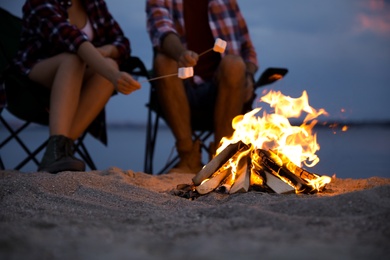 People roasting marshmallows over burning firewood on beach, closeup