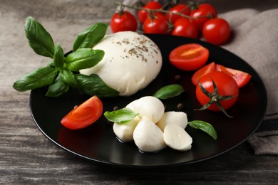 Photo of Delicious mozzarella with tomatoes and basil leaves on wooden table, closeup