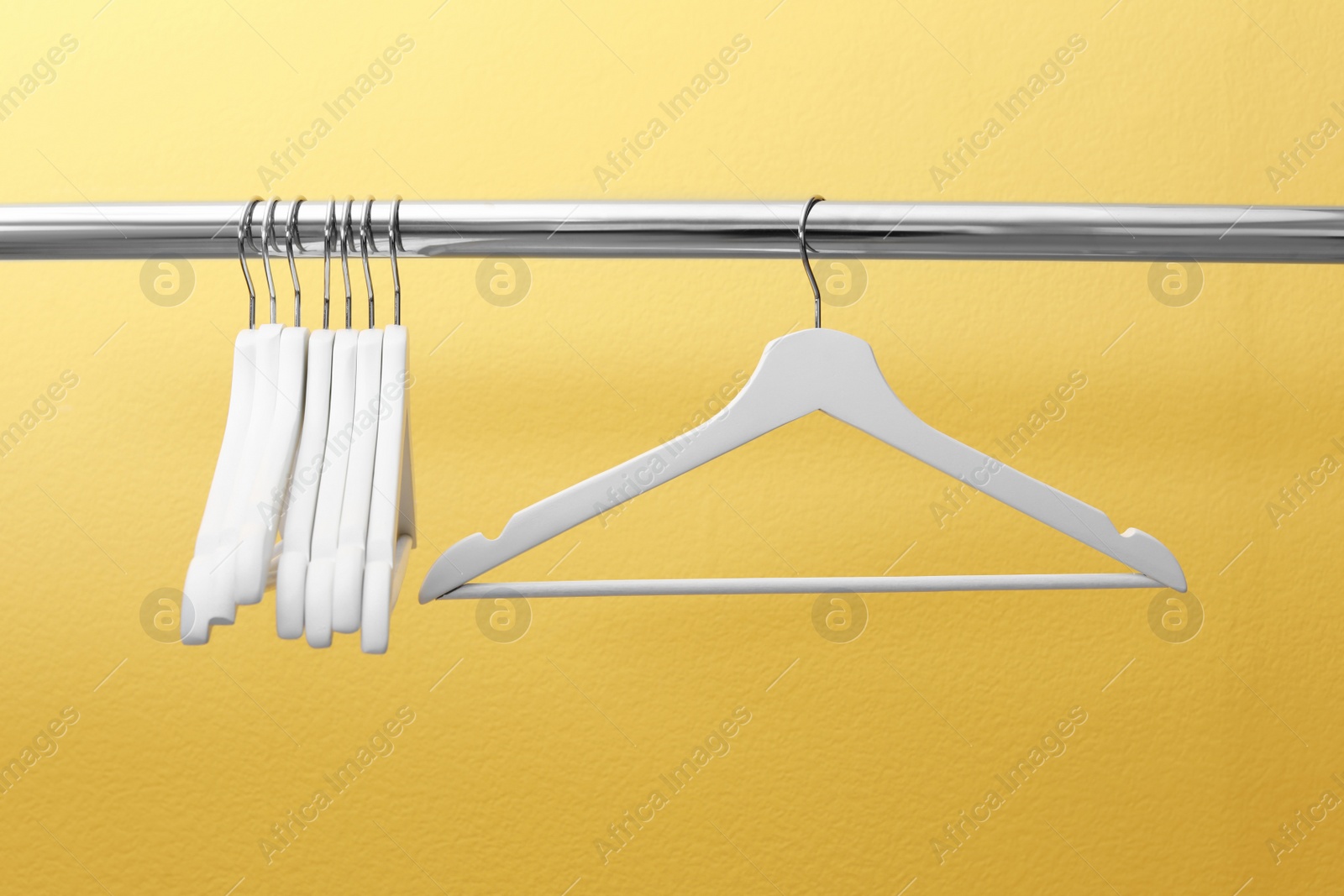 Photo of Clothes hangers on metal rail against color background