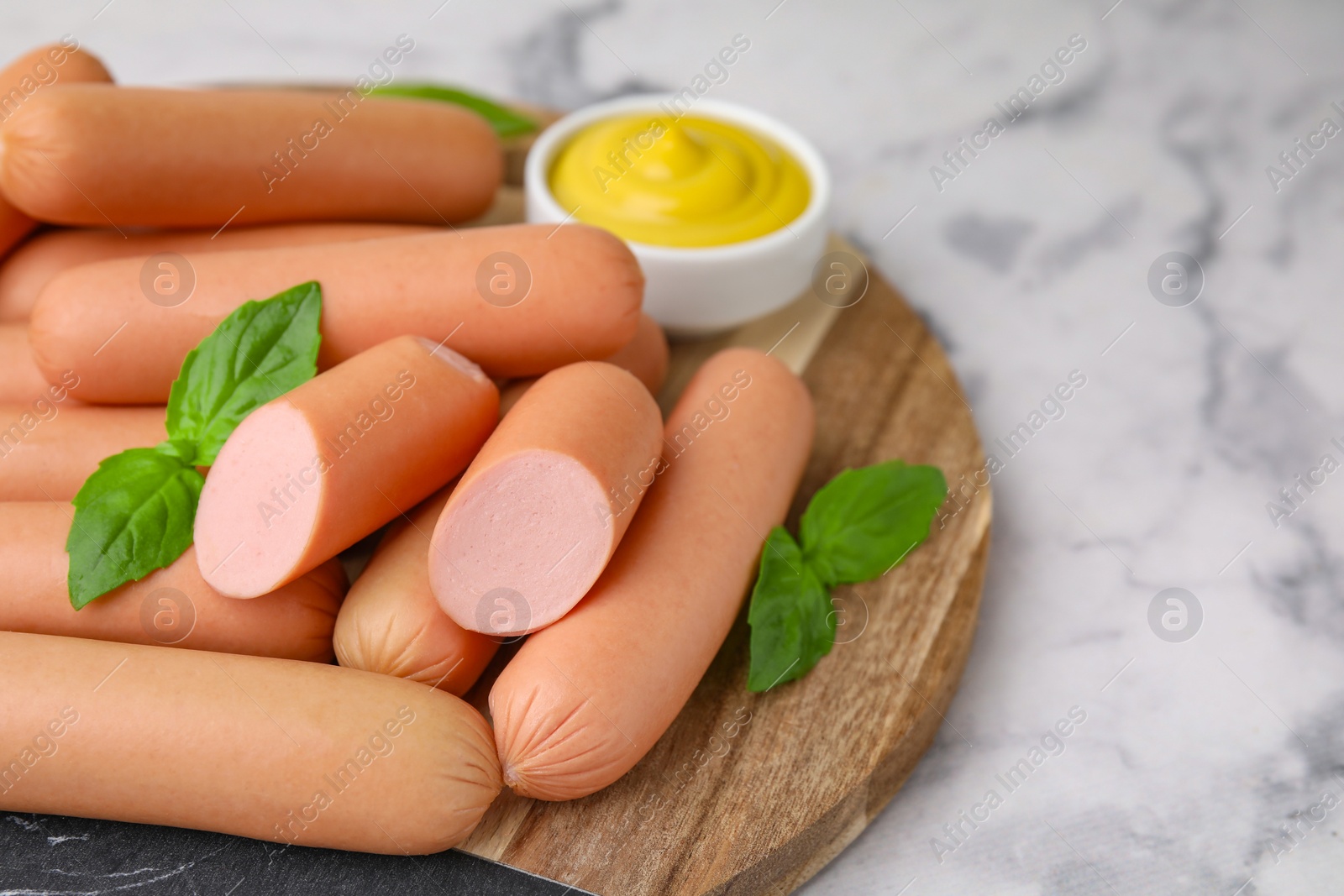 Photo of Delicious boiled sausages and basil on white marble table, closeup