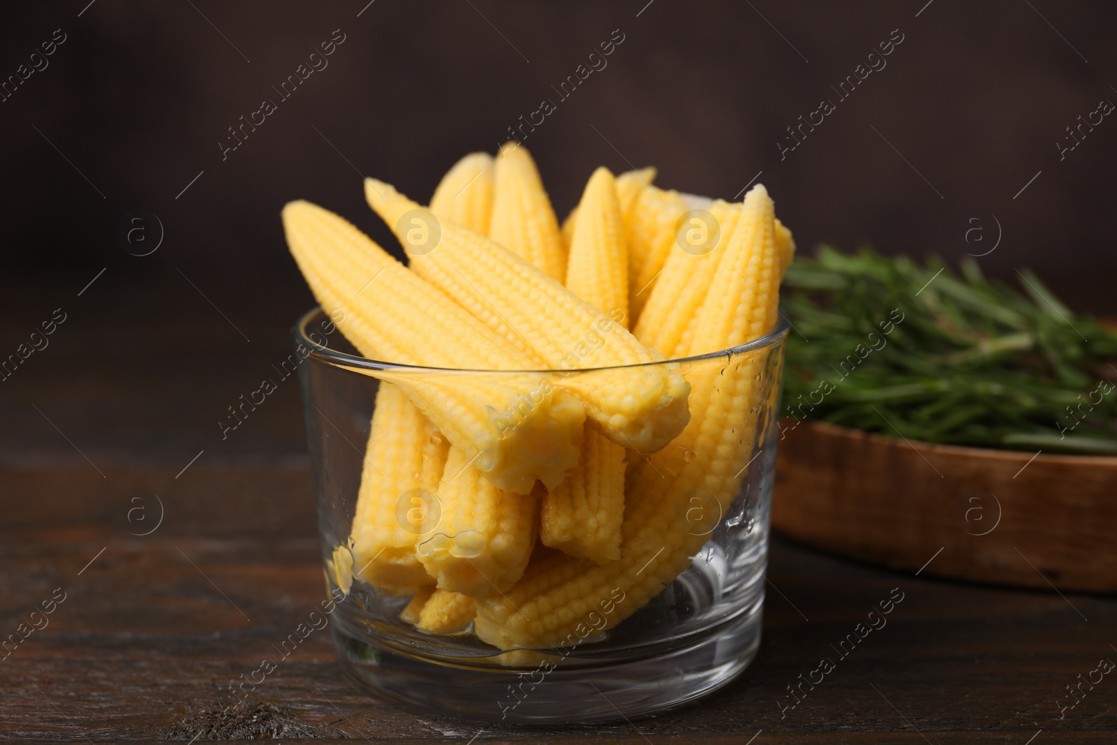 Photo of Tasty fresh yellow baby corns in glass on wooden table