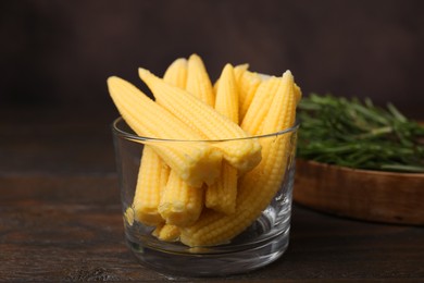 Photo of Tasty fresh yellow baby corns in glass on wooden table