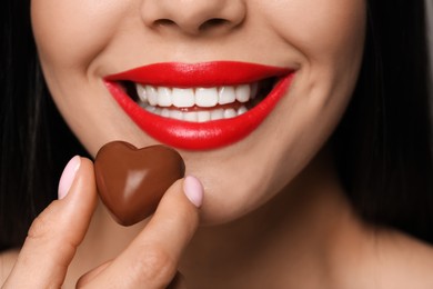 Photo of Young woman with red lips holding heart shaped chocolate candy, closeup