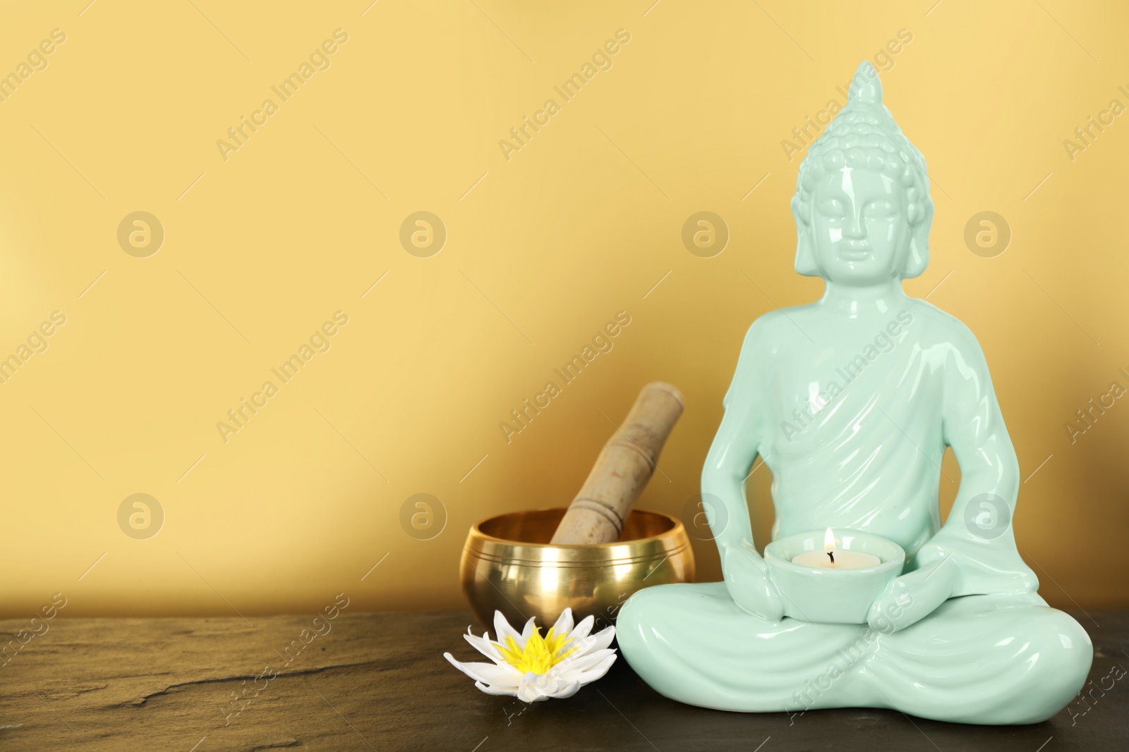 Photo of Buddha statue with burning candle near lotus flower and singing bowl on black table. Space for text