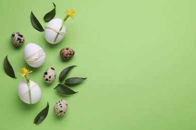 Photo of Festively decorated Easter eggs and leaves on green background, flat lay. Space for text
