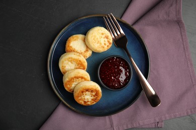 Delicious cottage cheese pancakes with jam on black table, top view
