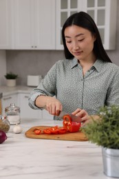 Cooking process. Beautiful woman cutting bell pepper at white marble countertop in kitchen