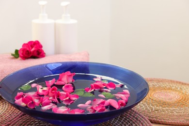 Pink roses, petals in bowl with water, cosmetic products and towel on table. Space for text