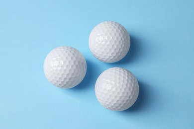 Three golf balls on light blue background, flat lay