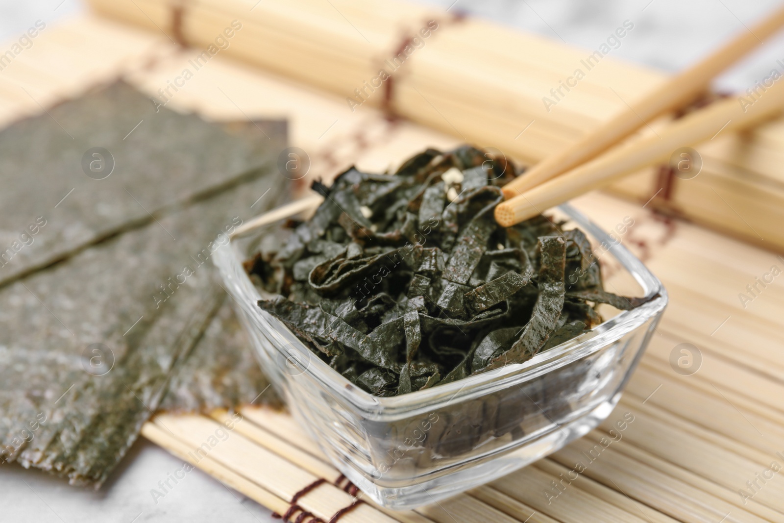 Photo of Chopped nori sheets with sesame and chopsticks on white table, closeup