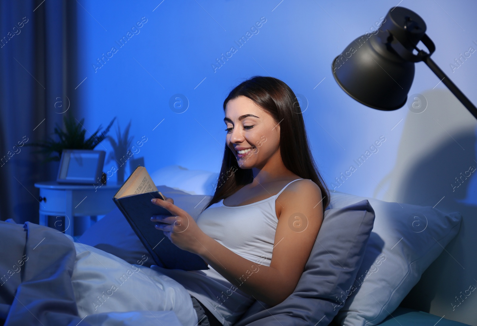 Photo of Young woman reading in dark room at night. Bedtime