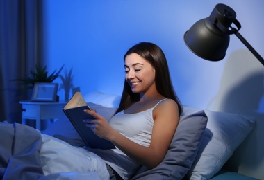 Young woman reading in dark room at night. Bedtime