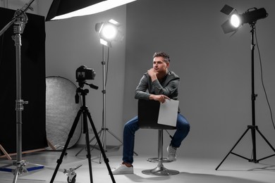 Photo of Casting call. Man with script sitting on chair and performing in front of camera in studio