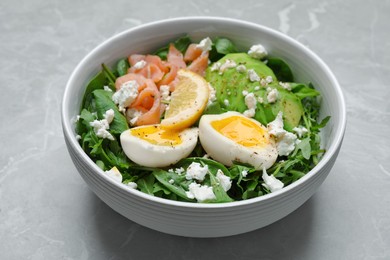 Delicious salad with boiled egg, salmon and cheese in bowl on light grey marble table, closeup