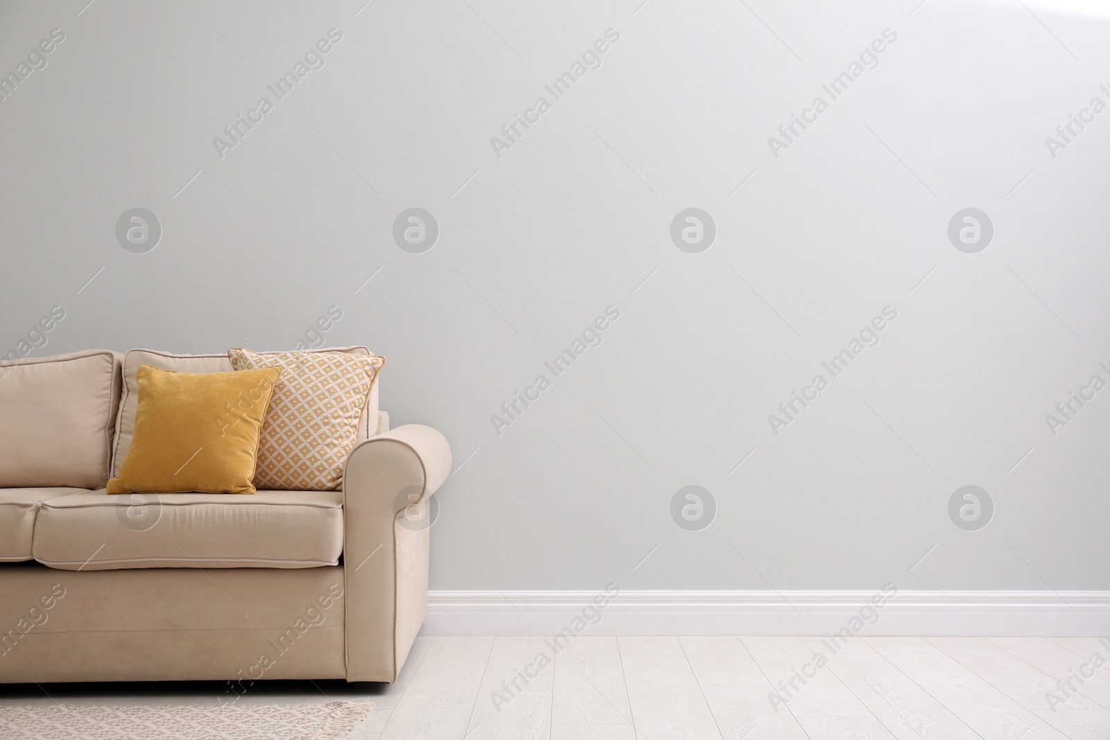 Photo of Comfortable beige sofa near light wall indoors, space for text. Simple interior