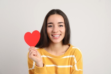 Photo of Portrait of beautiful young woman with paper heart on light background