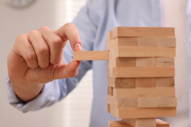 Playing Jenga. Man removing wooden block from tower indoors, closeup