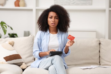 Confused woman with calculator and credit card planning budget at home. Debt problem