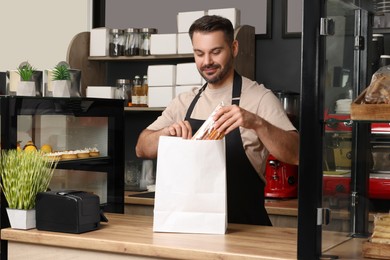Photo of Business owner in his cafe. Man putting pastry into paper bag at desk